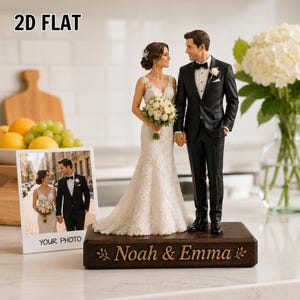 May include: A 3D wedding cake topper featuring a bride in a white lace gown and a groom in a black tuxedo standing on a dark wooden base engraved with the text Noah & Emma. Beside it is a 2D flat photo print of the same couple with the text YOUR PHOTO.