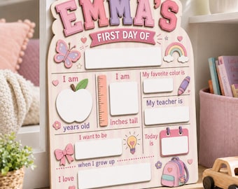 May include: A light-colored wooden sign for a first day of school with the name EMMA'S at the top. The board features blank white spaces for writing details like age, height, favorite color, teacher, future career, and date, decorated with icons.