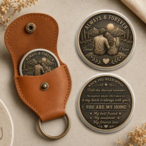Puede incluir: Un estuche para llavero de cuero color canela con cierre de broche que contiene una moneda de metal color bronce. Se muestran dos monedas metálicas redondas adicionales, una con una pareja junto a un lago con el texto ALWAYS & FOREVER, y la otra con el texto WHEN YOU NEED A HUG y YOU ARE MY HOME.