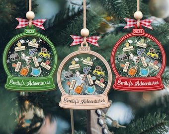 Puede incluir: Tres adornos navideños personalizados con forma de globo de nieve, cada uno con un marco de diferente color: verde, madera natural y rojo. Cada adorno presenta iconos temáticos de viajes y el texto "Emily's Adventures" y "2025".