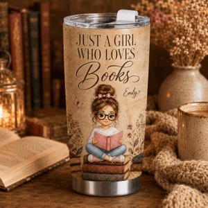 Pode incluir: Um copo de aço inoxidável com fundo bege estilo pergaminho apresentando o texto "JUST A GIRL WHO LOVES Books" e o nome "Emily". Uma ilustração mostra uma pessoa de óculos sentada sobre uma pilha de livros lendo um livro rosa.
