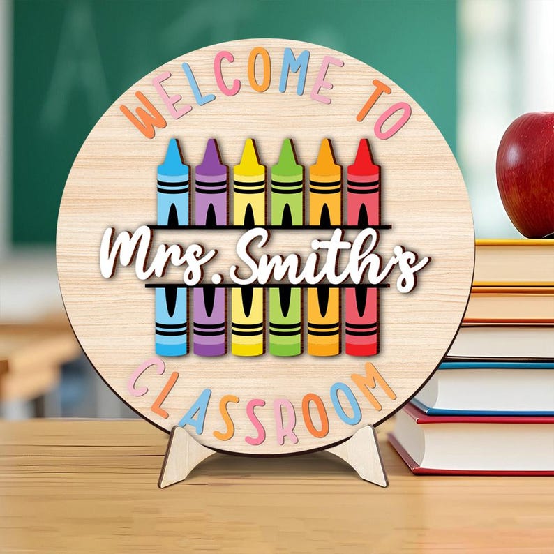 Może przedstawiać: Drewniany znak do klasy z napisem "WELCOME TO Mrs. Smith's CLASSROOM" w kolorowych literach. Znak przedstawia rząd kredek w r&oacute;żnych kolorach. Znak stoi na drewnianym stojaku.