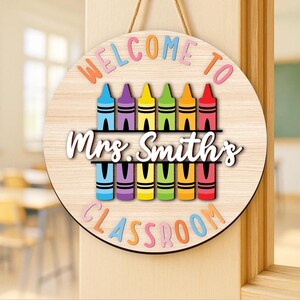Może przedstawiać: Okrągły drewniany znak z napisem "WELCOME TO Mrs. Smith's CLASSROOM" w kolorowych literach. Znak przedstawia rząd kredek w r&oacute;żnych kolorach, idealny do dekoracji klasy.