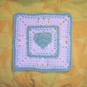 May include: A crocheted square with a heart design in the center. The square is made with white and light blue yarn.