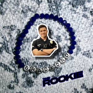 May include: A blue beaded bracelet with silver letter beads spelling "BRADFORD". A sticker of a man in a police uniform is in the center. The text "The Rookie" is at the bottom in blue.