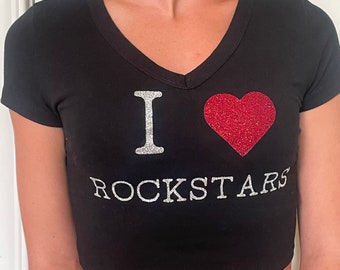 Op de afbeelding: Zwarte crop top met een V-hals. De tekst "I ROCKSTARS" staat op de voorkant. De letter "I" is in zilveren glitter, met een rode glitter hart ernaast. Het woord "ROCKSTARS" is ook in zilveren glitter.