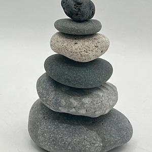 May include: A stack of smooth, gray stones of varying sizes, balanced atop one another. The top stone is dark gray, while the others range in color from light gray to a darker, greenish-gray. The arrangement suggests a natural, zen-like aesthetic.