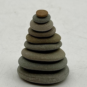 May include: A stack of smooth, gray and brown river stones arranged in a conical shape. The base consists of larger, flat stones, with each subsequent stone decreasing in size, culminating in a small, round, brown stone at the top. The stones are naturally weathered.