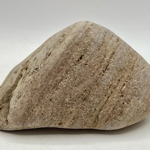 May include: A smooth, rounded stone with a light brown color and a textured surface. The stone has subtle variations in color and a natural, organic shape. Ideal for decorative purposes or as a natural element in crafts.