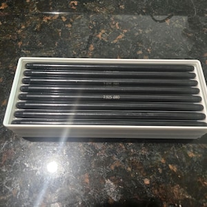 May include: A white rectangular tray filled with black metal rods. The rods are arranged in parallel rows. Some rods have the text "7.925-080" printed on them.