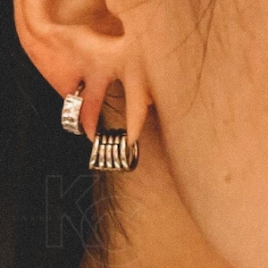 Könnte beinhalten: Nahaufnahme eines Ohrs mit zwei silbernen Creolen. Der Ohrring am unteren Ohrläppchen ist eine mehrlagige Creole, während der Ohrring am oberen Ohrläppchen eine einzelne, dünne Creole mit einem strukturierten Design ist.