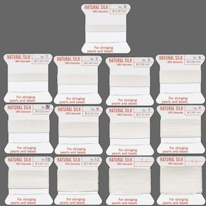May include: A set of 12 spools of natural silk thread for stringing pearls and beads. The spools are labeled with numbers 0 through 12 and the corresponding thread diameter in millimeters. The thread is white and the spools are white with red lettering.