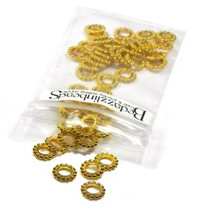 May include: A bag of gold-colored metal jump rings. The jump rings are small and have a beaded edge. The bag is labeled "Beadzillions Beads & Jewelry Supplies"