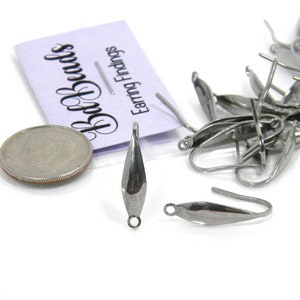 May include: A close-up of silver-toned earring findings. The findings are shaped like a teardrop with a small loop at the top. The findings are displayed on a white surface with a small coin for scale.