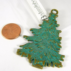 May include: A green and gold metal Christmas tree charm with a star on top. The charm is about the size of a US penny.