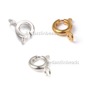 Puede incluir: Tres cierres de anillo de resorte en tonos plateados y dorados. Los cierres son redondos con un pequeño lazo y un mecanismo de resorte para un cierre seguro. Se utilizan para la fabricación de joyas y manualidades.
