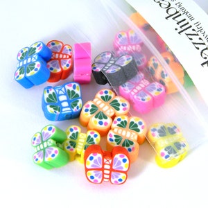Könnte beinhalten: Eine Tüte mit bunten, schmetterlingsförmigen Polymer Clay Perlen. Die Perlen sind in verschiedenen Farben, darunter Blau, Pink, Grün, Gelb und Orange. Die Perlen sind perfekt für die Herstellung von Schmuck, Schlüsselanhängern oder anderen Bastelarbeiten.