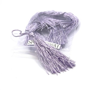 May include: A bundle of light purple tassels in a clear plastic bag. The tassels are made of thin, silky threads and are tied together at the top. A small tag with the text "Sparkle Beads & Jewels" is visible.