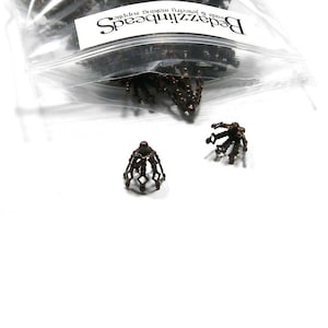May include: A close-up of a bag of small, copper-coloured metal bead caps. The caps are shaped like a crown or a flower with a pointed top and a round base. The bag is labelled "Beadzillions" and "Beads & Jewellery findings supplies".