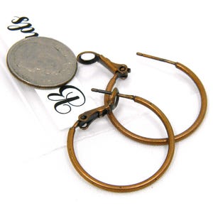 May include: A pair of copper-toned hoop earrings with a hinged closure. The earrings are approximately 1 inch in diameter.