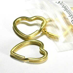 May include: A close-up of a package of gold heart-shaped key rings. The key rings are made of metal and have a smooth finish.
