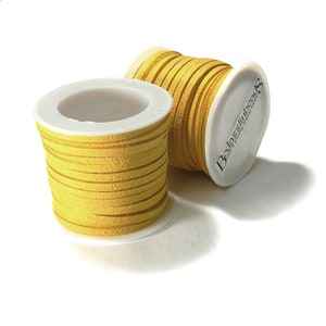 May include: Two spools of yellow suede leather cord. The cord is flat and wound around white spools. One spool is upright, and the other is tilted, revealing the brand name "Be dazzlin' beads".
