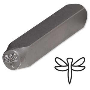 May include: A metal dragonfly stamp tool with a hexagonal handle. The stamp head features a detailed dragonfly design. The tool is gray and is designed for use in metal stamping and crafting projects.