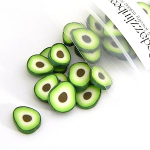 May include: A collection of avocado-shaped polymer clay beads. Each bead is a slice of avocado, featuring a dark brown pit, a white center, and a green outer layer. Some beads are loose, while others are in a clear plastic bag.