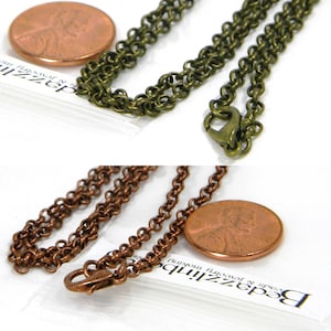 May include: Two antique bronze-colored chain necklaces with lobster clasps. One chain is a darker bronze, and the other is a lighter bronze. A U.S. penny is next to each chain for size comparison. The chains are on a white background.