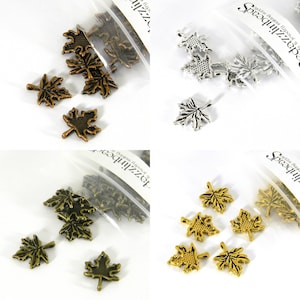 May include: Assortment of metal maple leaf charms in silver, gold, and copper finishes. The charms are packaged in clear plastic bags with the brand name "Spellbinder" printed on the bags.