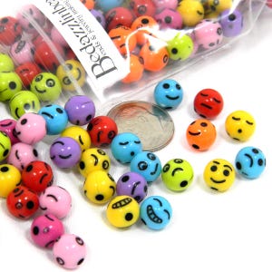 May include: A bag of colorful plastic smiley face beads. The beads are about the size of a dime. The bag is labeled "Beadzilla Beads & Jewelry High Quality".