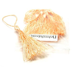 May include: A package of peach-colored silk tassels. The tassels are about 1 inch long and have a loop at the top for attaching. The package is labeled "Beadzinthebeadz Beads & Jewelry Making Supplies".