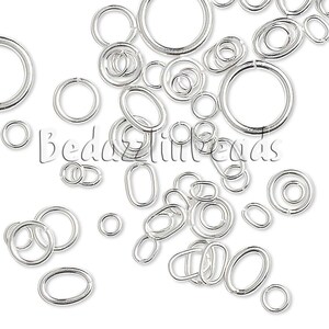 May include: A collection of silver-toned metal jump rings in various sizes and shapes, including circular and oval forms. The rings feature a smooth, reflective finish and are scattered across the frame, with the text BedazzledBeads visible.