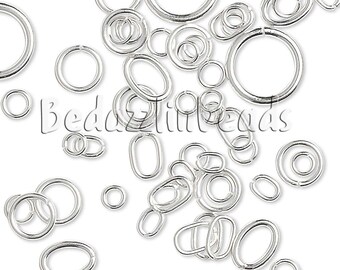 May include: A collection of silver-toned metal jump rings in various sizes and shapes, including circular and oval forms. The rings feature a smooth, reflective finish and are scattered across the frame, with the text BedazzledBeads visible.