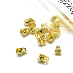 May include: A close-up of a bag of gold-colored metal clasps. The clasps are small and have a round shape with two holes on each side. They are designed to be used for jewelry making.