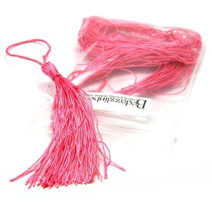 May include: A pink tassel with a loop at the top. The tassel is made of thin strands of yarn and is about 2 inches long. The tassel is packaged in a clear plastic bag with a label that reads "Beadzzilibe Beads & Jewelry Made in the USA".