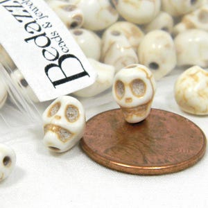 8 pequeñas cuentas de 8 mm de imitación de hueso, color beige y marrón, con forma de calavera de esqueleto, pequeñas cuentas de piedra craquelada color marfil y orificio para ensartar.