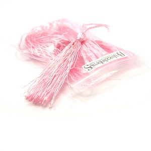 May include: A bag of pink silk tassels, with the brand name "SparkleBeads" printed on the bag. The tassels are made of soft, silky material and are perfect for adding a touch of elegance to any project.