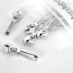 May include: A close-up of a pack of silver-toned wrench charms. The charms are in the shape of adjustable wrenches and have a detailed design.