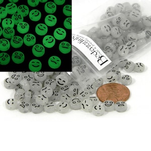 May include: A bag of glow-in-the-dark plastic beads with different smiley face expressions. The beads are white with black details and are approximately 1 cm in diameter. The bag is labeled "Bedazzlin' Beads & Jewelry Mesquite".