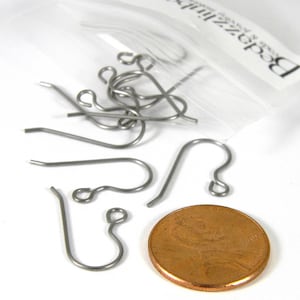 May include: A close-up of a pile of silver earring hooks, next to a US penny. The hooks are about the size of a penny.