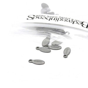 Pode incluir: Um close-up de uma bolsa de pingentes de metal ovalados prateados com as palavras "S.Steel" gravadas neles.