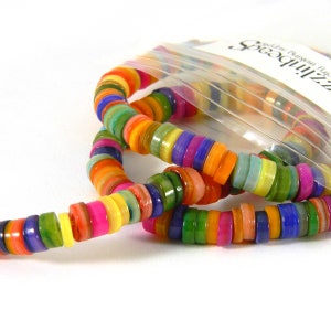 May include: A colorful strand of round, flat, multi-colored shell beads. The beads are arranged in a rainbow pattern and are strung on a clear thread. The beads are in a plastic bag with the text "Zilli Beads" printed on the bag.