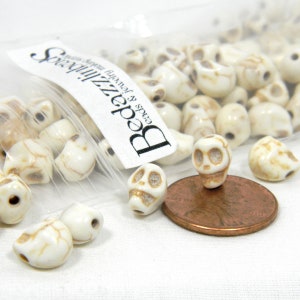 May include: A bag of white ceramic skull beads with brown detailing. The beads are about the size of a US penny.