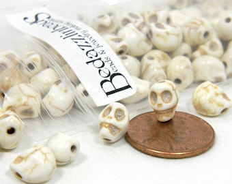May include: A bag of white ceramic skull beads with brown detailing. The beads are about the size of a UK penny.