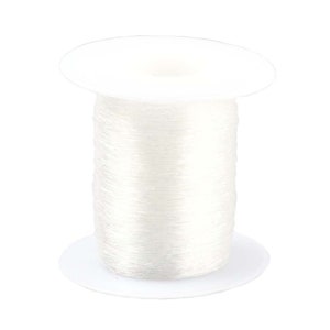 May include: A spool of clear elastic thread wound around a white plastic bobbin.