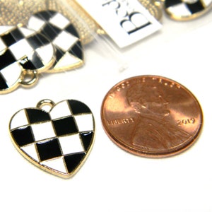 May include: A close-up of a black and white checkered heart charm. The charm is made of metal and has a gold finish. The charm is about the size of a US penny.