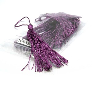 May include: A bag of purple tassel trim, with one tassel pulled out of the bag. The bag has a label that says "Little Beads".