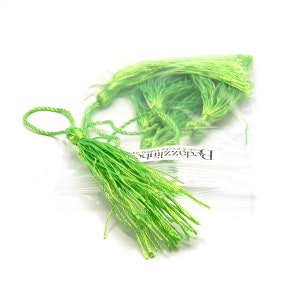 May include: A bag of lime green tassels with a single tassel hanging out of the bag. The bag has the text "Beadzzilious" and "cards & jewelry for the budget fashionista" printed on it.
