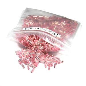 May include: A clear plastic bag filled with pink glass seed beads. The bag is open and the beads are spilling out. The bag has a label that says "Beadzilla" and "Made in Taiwan".